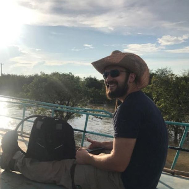 JCU Education student Connor Wolf smiling and sitting on a boat as he tours a lake in Cambodia. 