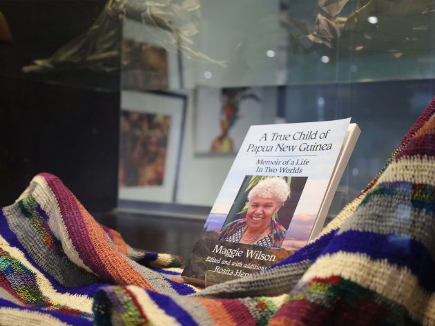Maggie Wilson's memoir, A True Child of P.N.G. in a glass exhibition case, surrounded by Maggie's multi-coloured shawl. 