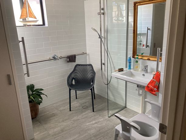 A open floor plan bathroom with a chair in shower and stool for toilet. 